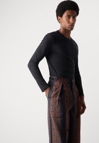 Top negro de manga larga combinado con pantalones azules estampados que presentan acentos florales naranjas y pliegues, mostrando un ajuste entallado y elegante.
