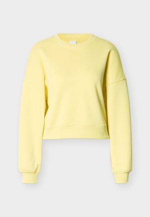 Gul kort hettegenser laget av mykt stoff. Har ribbekant, senkede skuldre og en enkel, ren halslinjedesign.