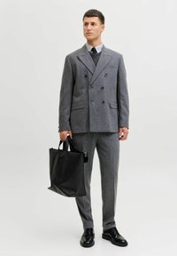 Hall hall kahekordse nööbistusega ülikonnajakk ja sobivad püksid, kombineeritud triibulise särgi ning musta lipsuga. Mustast nahast käekott, läikivad jalatsid.