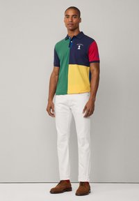 Polo-shirt met een color-block ontwerp in groen, geel, marineblauw en rood; van katoen; een getailleerde stijl; gecombineerd met witte broeken en bruine schoenen.