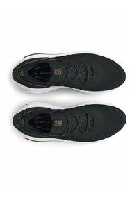 Chaussures de sport noires avec une tige texturée, semelle blanche contrastante, col rembourré et accents jaunes sur la marque et la zone des lacets.