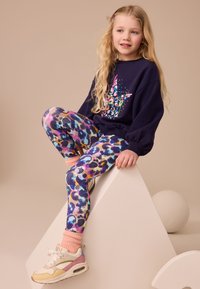 Purple sweatshirt with colorful floral design, paired with multi-colored patterned leggings. Also features light pink socks and beige sneakers.