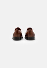 Zapatos de vestir de cuero marrón con un acabado liso, puntera redondeada y tacón bajo; costuras mínimas y un sutil logo en el tacón.