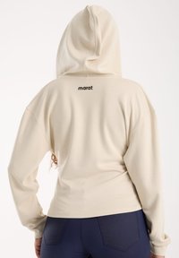 Kermanvärinen huppari, joka on valmistettu pehmeästä kankaasta. Siinä on kengurupockets ja nyöritettävä huppu. Takana on 'marat'-logo.