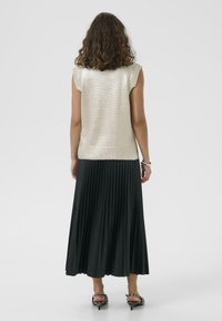 Kultainen metallinhohtoinen hihaton toppi, jossa on ribbikuvio, yhdistettynä pitkään, laskostettuun mustaan hameeseen ja kuviollisiin remmisandaaleihin.