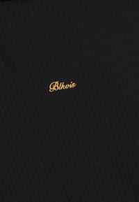 Zwart ribstof met kleine, gecentreerde gouden geborduurde tekst "Blkvis" in een cursieve lettertype.