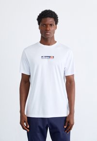 Fehér, rövid ujjú póló sima anyagból, az elején színes "ellesse" logóval, kerek nyakkivágással és laza fazonnal.