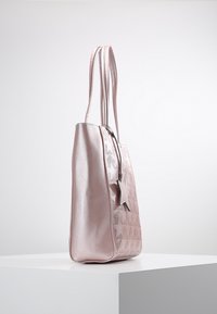 Rosa metallisk tote-väska med en slät yta, utskurna mönster och en stjärnformad charm. Har långa axelremmar för enkel bärande.