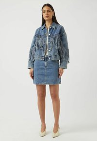 Vaaleansininen farkkutakki, jossa hihan reunassa hapsut, yhdistetty samaa sarjaa olevaan minihameeseen. Valkoinen toppi alla ja neutraalin väriset korkokengät viimeistelevät asun.