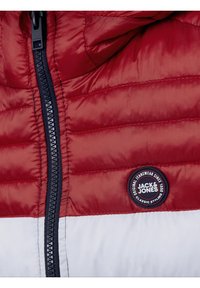 Röd och vit vadderad jacka med svart dragkedja och rund Jack & Jones-logotyp på höger sida.