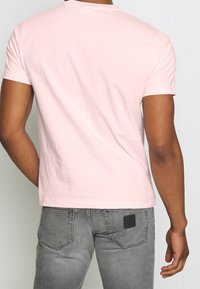 Camiseta de manga corta color rosa claro con cuello redondo clásico, confeccionada en tejido suave, combinada con jeans de mezclilla gris claro.