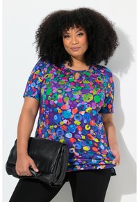 Lilla kortærmet top med et flerfarvet prikmønster, med en nøglehul-udskæring. Kombineret med en sort clutch og leggings.
