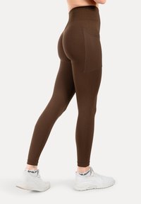 Bordeaux hoge taille leggings met een gestructureerd, diamantpatroon en een zijzak. Gepaard met witte sportschoenen.