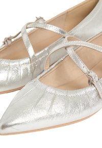 Ballerines en métal argenté avec des pointes effilées, un design à sangle croisée et une texture plissée sur la zone des orteils. Doublure intérieure lisse.