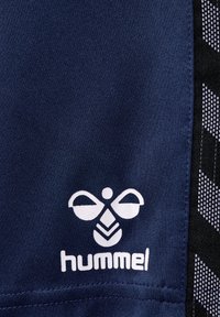 Donkerblauwe stoffen shorts met een wit logo met een abstract ontwerp en de tekst "hummel." Het zijpaneel bevat een zwart geometrisch patroon.