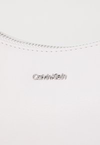 Pink leather bag with a smooth texture, featuring a silver zipper and a metallic Calvin Klein logo on the side.