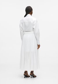 Fehér hosszúujjú ing, fehér plisszelt szoknyával. Szigorúan kivágott gallérral, rugalmas derékkal és áttetsző anyaggal rendelkezik. Fekete magassarkú cipővel viselik.