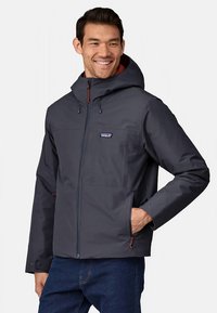Patagonia men's jacket in dark navy, made from water-resistant material. Features a zip closure, hood, and multiple pockets.
