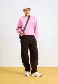 Oversized rosa Sweatshirt, dunkelbraune Leopard-Print-Hosen, weiße Sneakers und eine beige Cap. Strukturierter Stoff und lässige Passform.