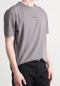 Grå bomull T-shirt med korta ärmar och rund halsringning, med en liten svart "BOSS"-logotyp på bröstet. Bärs med mörka byxor.