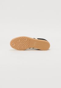 Svart sneaker med en strukturerad överdel, gummisula med fiskbensmönster och en präglad logotype på hälen.