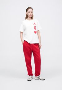 Biała bawełniana koszulka z czerwonym nadrukiem, zestawiona z czerwonymi spodniami dresowymi. Sneakersy z subtelną fakturą i czarną podeszwą. Prosty, luźny krój.