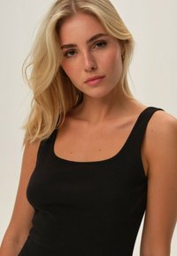 Black ribbed tank top with a square neckline and thin straps, made of soft fabric, featuring a fitted silhouette and slight stretch.