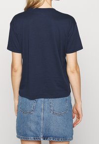 Camiseta de algodón azul marino con un corte relajado y manga corta, llevada con una falda de mezclilla que cuenta con bolsillos traseros y un dobladillo deshilachado.