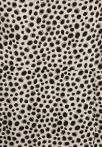 Mustaa ja harmaata pilkullista kangasta beigen taustan päällä. Pisteet vaihtelevat koossa ja ovat järjestetty satunnaisesti, ja niillä on sileä pinta.
