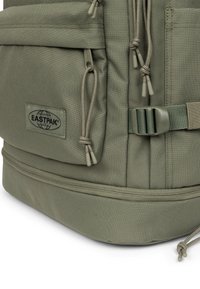 La mochila verde Eastpak presenta un tejido duradero, múltiples bolsillos con cremallera, correas ajustables y un prominente parche con el logotipo. Superficie texturizada.