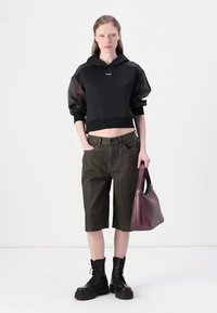 Μαύρο κοντό hoodie με διαφανή μανίκια, ελιάς χρώματος κοντές σορτς μέχρι το γόνατο, μαύρες μπότες με κορδόνια και μπορντώ τσάντα χειρός με δομημένο σχήμα.