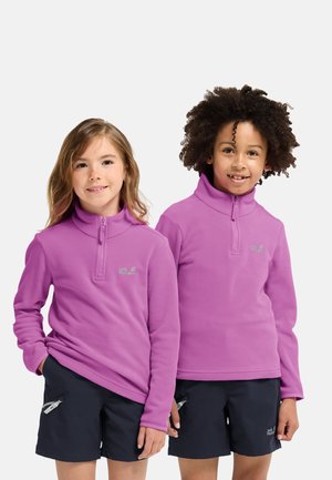 Zwei Kinder tragen leuchtend violette Fleecepullover mit Reißverschluss am Hals und Logo auf der Brust, kombiniert mit dunklen Shorts mit Reißverschlusstaschen.
