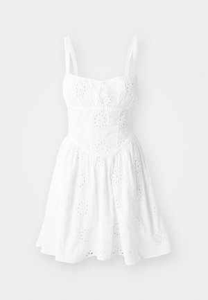 Robe blanche avec des bretelles spaghetti réglables, un corsage ajusté et une jupe évasée. Présente une broderie en œillets et un détail à cordon au niveau du décolleté.