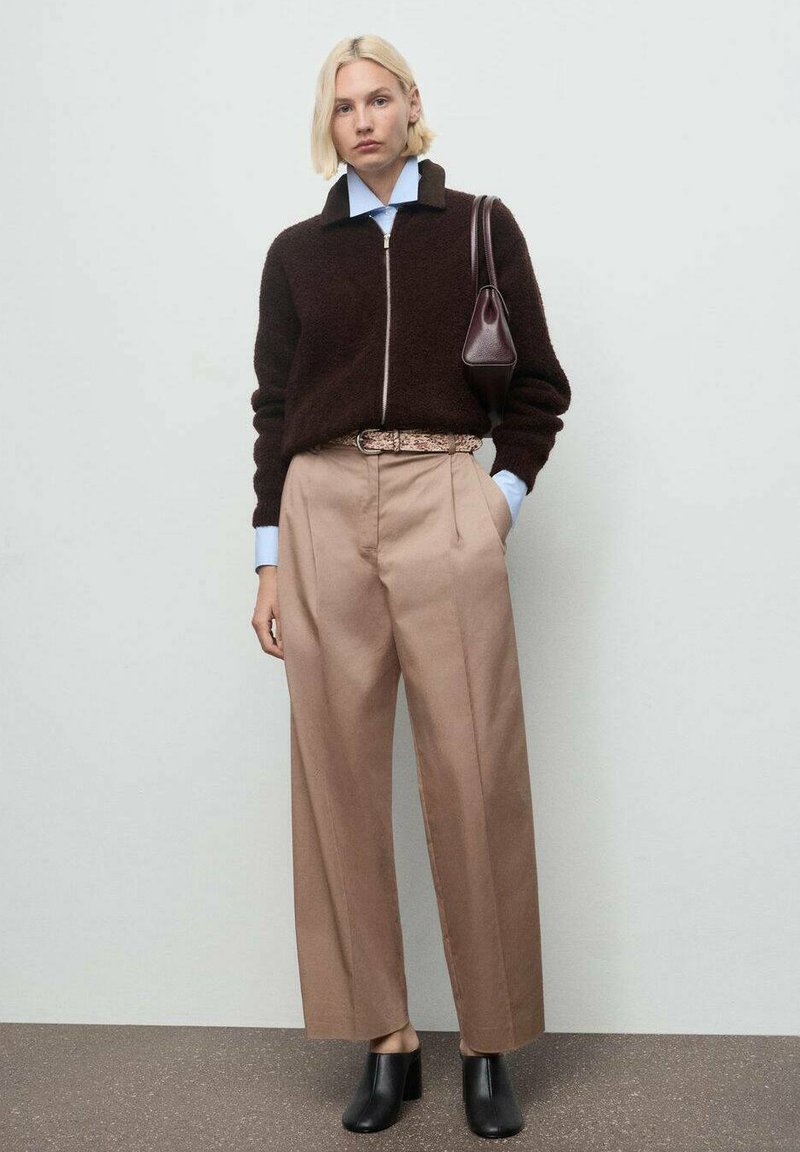 Bruine ritssluiting fuzzy sweater, lichtblauwe collared shirt, beige hooggeplaatste broek met plooien, zwarte hoge laarzen en een kleine bruine handtas.