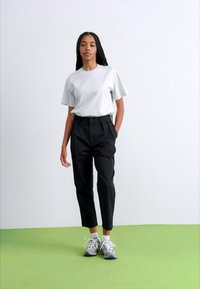 T-shirt gris à manches courtes, pantalon noir taille haute et baskets grises. Tissu lisse, coupe décontractée et design de jambe fuselée.