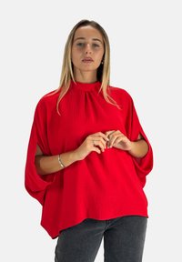 Rote, locker sitzende Bluse mit hohem Kragen und kurzen Ärmeln. Hergestellt aus strukturierter Stoff mit Faltenlegung am Ausschnitt.