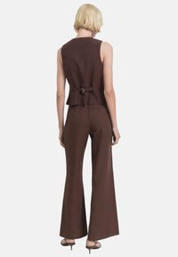Bruine mouwloze top met een peplum taille, gecombineerd met bijpassende hoge taille flared broeken. Glad stoffen textuur, minimalistisch ontwerp.