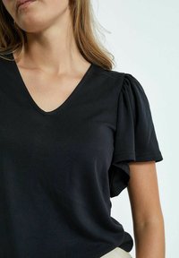 Must jõhvikavari, millel on V-kaelus ja puhvis varrukad, on valmistatud pehmest kangast, millel on sile tekstuur. Lihtne ja minimalistlik disain.