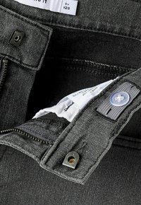 Donkergrijze spijkerbroek met rits, metalen drukknop, verstelbare taillebandknop en gedeeltelijk zichtbaar kledinglabel aan de binnenkant.