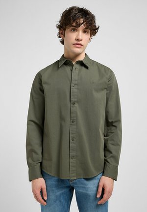 Camisa de botones en verde oliva, hecha de una tela suave, con un collar estructurado, mangas largas y un sutil logo bordado en el pecho.