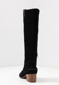 Knee-high black suede boot with a side zipper, stacked wooden heel, and decorative stitching along the edge and heel.