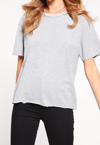 Graues Kurzarm-T-Shirt aus einem Baumwollgemisch, mit Rundhalsausschnitt und offenen Säumen, kombiniert mit schwarzen Hosen.