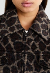 Leopardmönstrad jacka med en brun och svart färgskala, dragkedja framtill och kragen är gjord av ett texturerat tyg.