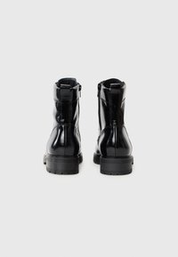 Bottes noires en cuir à la cheville avec une finition brillante, fermeture éclair sur le côté, talon renforcé et semelle en caoutchouc texturée. Vue arrière montrée.