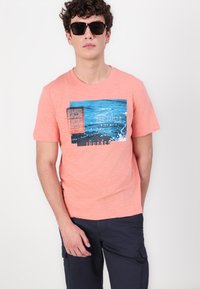 Koralfarvet polyester t-shirt med trykt rektangulært motiv, der viser blåt vand og tekst, rund halsudskæring, korte ærmer og loose fit.