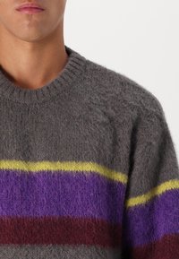 Szürke kötött pulóver vízszintes csíkokkal lila, sárga és burgundi színben. Puha, bolyhos anyagból készült, kerek nyakkal.