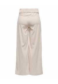 Pantalons larges beiges en tissu côtelé, dotés d'une taille élastique, avec une coupe décontractée et une texture lisse.