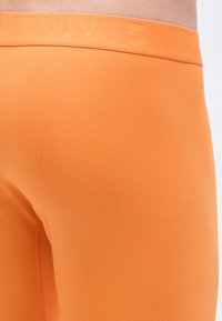 Oranžové športové šortky s textúrovanou tkaninou, na páse s vypuklým logom. Dizajn je priliehavý a bezšvový.