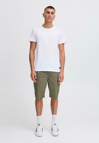 Camiseta de algodón blanca combinada con pantalones cortos cargo verde oliva con bolsillos laterales, completada con zapatillas blancas y calcetines de longitud media.