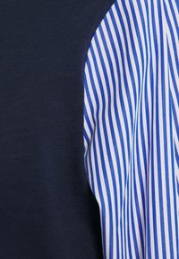 Närbild av marinblått tyg intill vitt tyg med vertikala blå ränder, som framhäver textur och kontrast mellan materialen.